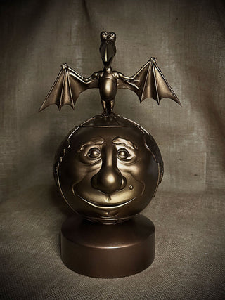 Bronze sculpture of a face with bat-like wings on a dark background
